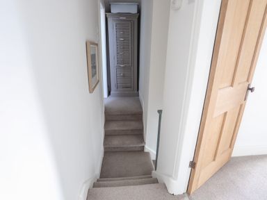 A narrow carpeted staircase leading to a hallway with a gray storage cabinet at Ty Llwyd in Trearddur Bay