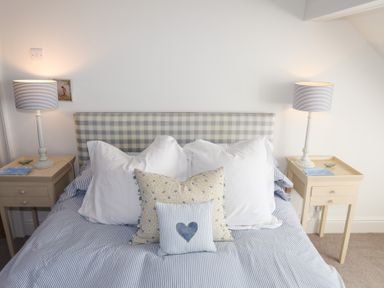 A bedroom with a checkered headboard two bedside tables with lamps and decorative pillows on the bed at Ty Llwyd in Trearddur Bay