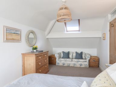 A bedroom with a wooden chest of drawers a floral sofa with pillows and a skylight window at Ty Llwyd in Trearddur Bay