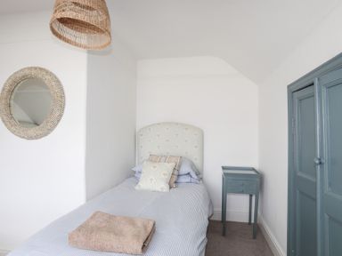 A bedroom with a single bed a side table a round wall mirror and a folded towel on the bed at Ty Llwyd in Trearddur Bay