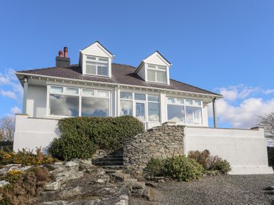 A white house with large windows and a stone staircase leading to the entrance at Ty Llwyd in Trearddur Bay