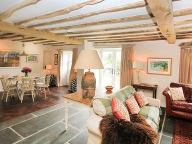 A living room and dining area with wooden beams on the ceiling and stone flooring at Ty Mawr Porthmadog in Porthmadog