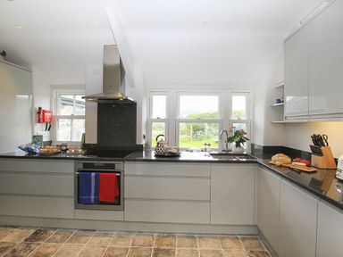 A kitchen with black countertops white cabinets a stove a kettle and bread on the counter at Ty Mawr Porthmadog in Porthmadog