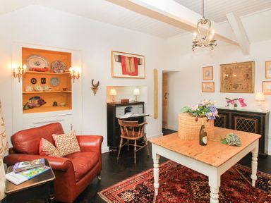 A sitting room with a red leather armchair beside a wooden table with flowers and a bottle at Ty Mawr Porthmadog in Porthmadog