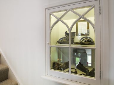 A display cabinet with old boots and plates on shelves near a staircase at Ty Mawr Porthmadog in Porthmadog