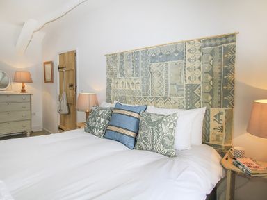 A bedroom with a bed with patterned cushions and a tapestry headboard two bedside tables with lamps a wooden door and a chest of drawers with a mirror at Ty Mawr Porthmadog in Porthmadog
