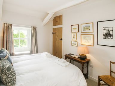 A bedroom with a bed, pillows, window with curtains, wooden door, framed pictures on the wall, bedside table with lamp, and a chair at Ty Mawr Porthmadog in Porthmadog