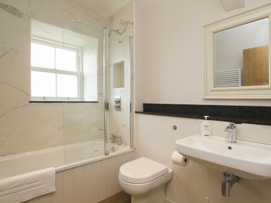 A bathroom with a bathtub and shower, toilet, sink with soap dispenser and a mirror at Ty Mawr Porthmadog in Porthmadog