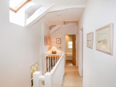 A hallway with a white railing a wooden table lamp framed pictures and an open door to a bathroom at Ty Mawr Porthmadog in Porthmadog