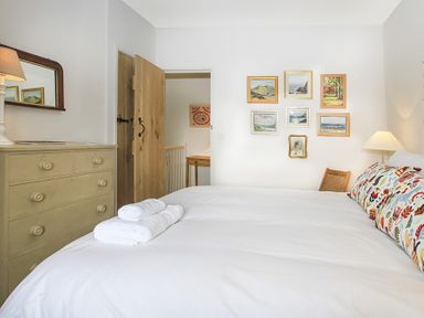 A bedroom with a bed with white linens and floral pillows a dresser a lamp wall art and an open wooden door at Ty Mawr Porthmadog in Porthmadog