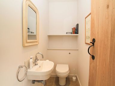 A small bathroom with a white sink and mirror on the left and a white toilet on the right with shelves above a door on the right with a black handle at Ty Mawr Porthmadog in Porthmadog