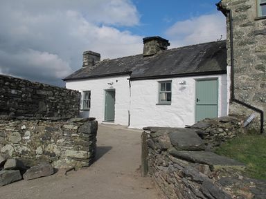 A stone cottage with white walls and green doors and windows surrounded by stone walls at Ty Mawr Porthmadog in Porthmadog