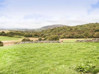 A grassy field with a stone wall and trees on hills in the background at Ty Mawr Porthmadog in Porthmadog