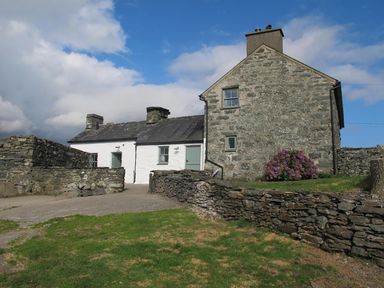 Stone and white painted houses with green doors and stone walls surrounding a grassy yard at Ty Mawr Porthmadog in Porthmadog