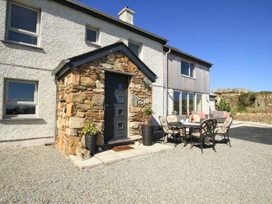 A house exterior with a stone porch and outdoor dining table with chairs on gravel at Ty Nant in South Stack