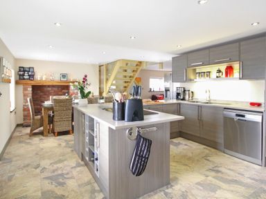 A modern kitchen with an island and dining table with wicker chairs at Ty Nant in South Stack