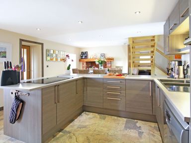 A kitchen with wooden cabinets a countertop with a knife holder and stove a dining area with chairs and flowers at Ty Nant in South Stack