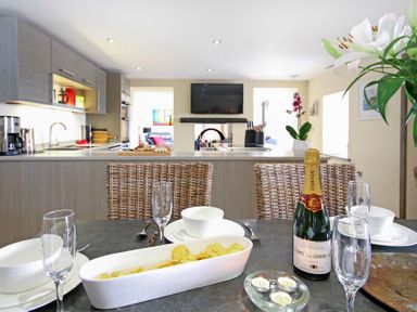 A kitchen and dining area with wicker chairs champagne bottle and snacks at Ty Nant in South Stack