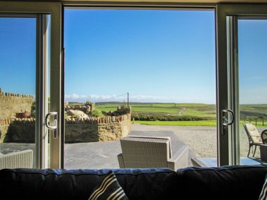A view through glass doors showing outdoor chairs and a stone wall with fields in the distance at Ty Nant in South Stack