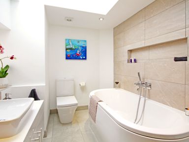 A bathroom with a bathtub a toilet a sink and a colorful painting above the toilet at Ty Nant in South Stack