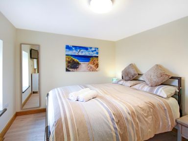A bedroom with a large bed with striped bedding a mirror on the wall and a beach path picture above the bed at Ty Nant in South Stack
