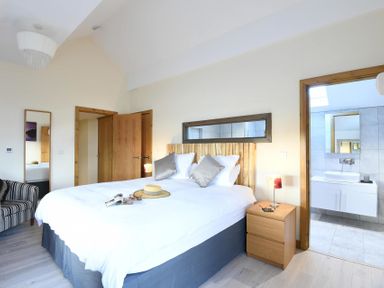 A bedroom with a bed bedside tables an armchair and an open door leading to a bathroom at Ty Nant in South Stack