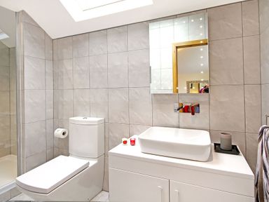 A bathroom with a white toilet a sink on a white cabinet a mirror above the sink and a glass shower enclosure at Ty Nant in South Stack