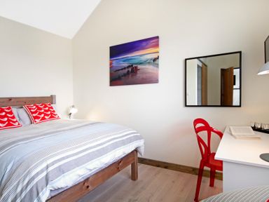 A bedroom with a wooden bed with red pillows a white desk with a red chair and a mirror on the wall at Ty Nant South Stack