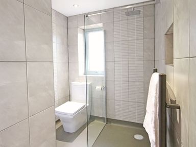 A bathroom with a toilet shower area with glass partition towel hanging on rack and window at Ty Nant in South Stack