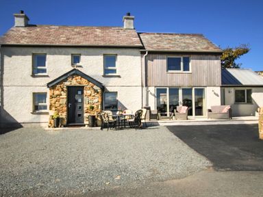 Exterior of a two-story house with stone and wood facade featuring outdoor seating at Ty Nant in South Stack