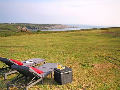 Two reclining lounge chairs with cushions and a small table with drinks on a grassy lawn with a coastal view at Ty Nant in South Stack