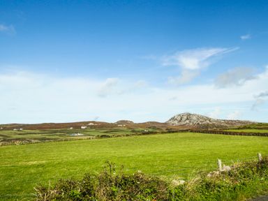 A grassy field with fences and hills under a blue sky at Ty Nant in South Stack
