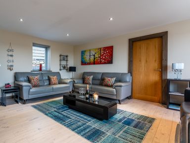 A living room with two gray sofas a colorful painting a blue patterned rug and a black coffee table at Ty Nant in South Stack