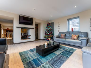 A living room with leather sofas a coffee table a decorated Christmas tree and a wall mounted TV at Ty Nant in South Stack