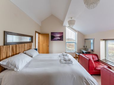 A bedroom with a large bed towels on the bed red chairs a wooden door a desk with a mirror and windows at Ty Nant in South Stack