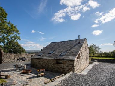 A stone cottage with skylights surrounded by gravel and a stone patio with outdoor furniture at Tyn Llwyn Cornel in Beddgelert