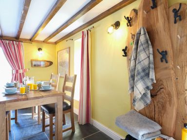 A dining area with a wooden table set for breakfast and a coat rack with a plaid scarf at Tyn Llwyn Cornel in Beddgelert