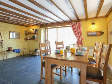 A dining room with a wooden table and six chairs set with bowls and glasses of orange juice at Tyn Llwyn Cornel in Beddgelert