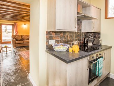 A kitchen with a stove oven fruit basket and orange juice next to a living room with a sofa at Tyn Llwyn Cornel in Beddgelert