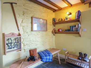A corner of a room with a wooden bench holding binoculars and a blue plaid blanket at Tyn Llwyn Cornel in Beddgelert
