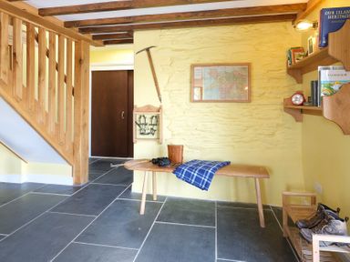 An entrance area with wooden stairs a bench with binoculars and a blue blanket hiking boots on a rack and shelves with books at Tyn Llwyn Cornel in Beddgelert