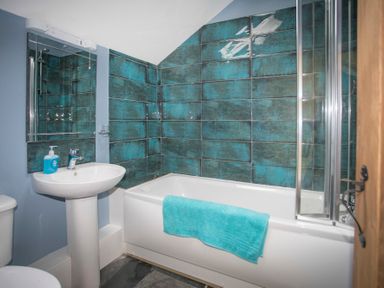 A bathroom with a white sink and bathtub with turquoise tiles on the wall at Tyn Llwyn Cornel in Beddgelert
