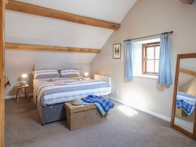 A bedroom with a double bed bedside tables a wicker chest and a mirror at Tyn Llwyn Cornel in Beddgelert
