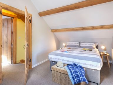 A bedroom with a double bed bedside tables with lamps and a wicker chest with a hat and a blanket at Tyn Llwyn Cornel in Beddgelert