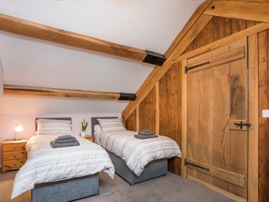 A bedroom with two single beds bedside tables and wooden wall and door at Tyn Llwyn Cornel in Beddgelert