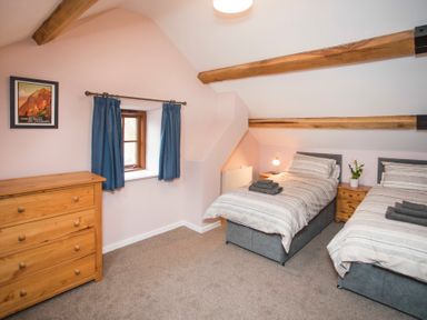 A bedroom with two single beds a wooden chest of drawers and a window with blue curtains at Tyn Llwyn Cornel in Beddgelert