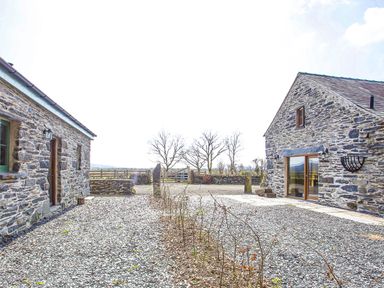 An outdoor courtyard with gravel ground between two stone buildings at Tyn Llwyn Cornel in Beddgelert