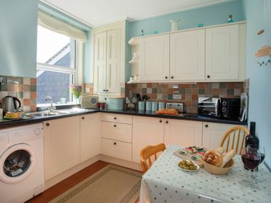 A kitchen with cream cabinets a washing machine a microwave and a table set with bread olives and wine at 17 Victoria Terrace - Perthi in Nantlle