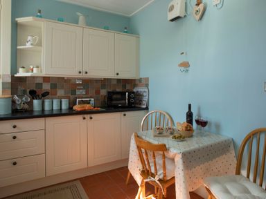 A kitchen with cream cabinets a tiled backsplash a table with food and two wooden chairs at 17 Victoria Terrace - Perthi in Nantlle