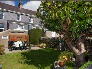 A backyard garden with a tree and outdoor dining set under an umbrella next to a stone wall at 17 Victoria Terrace - Perthi in Nantlle
